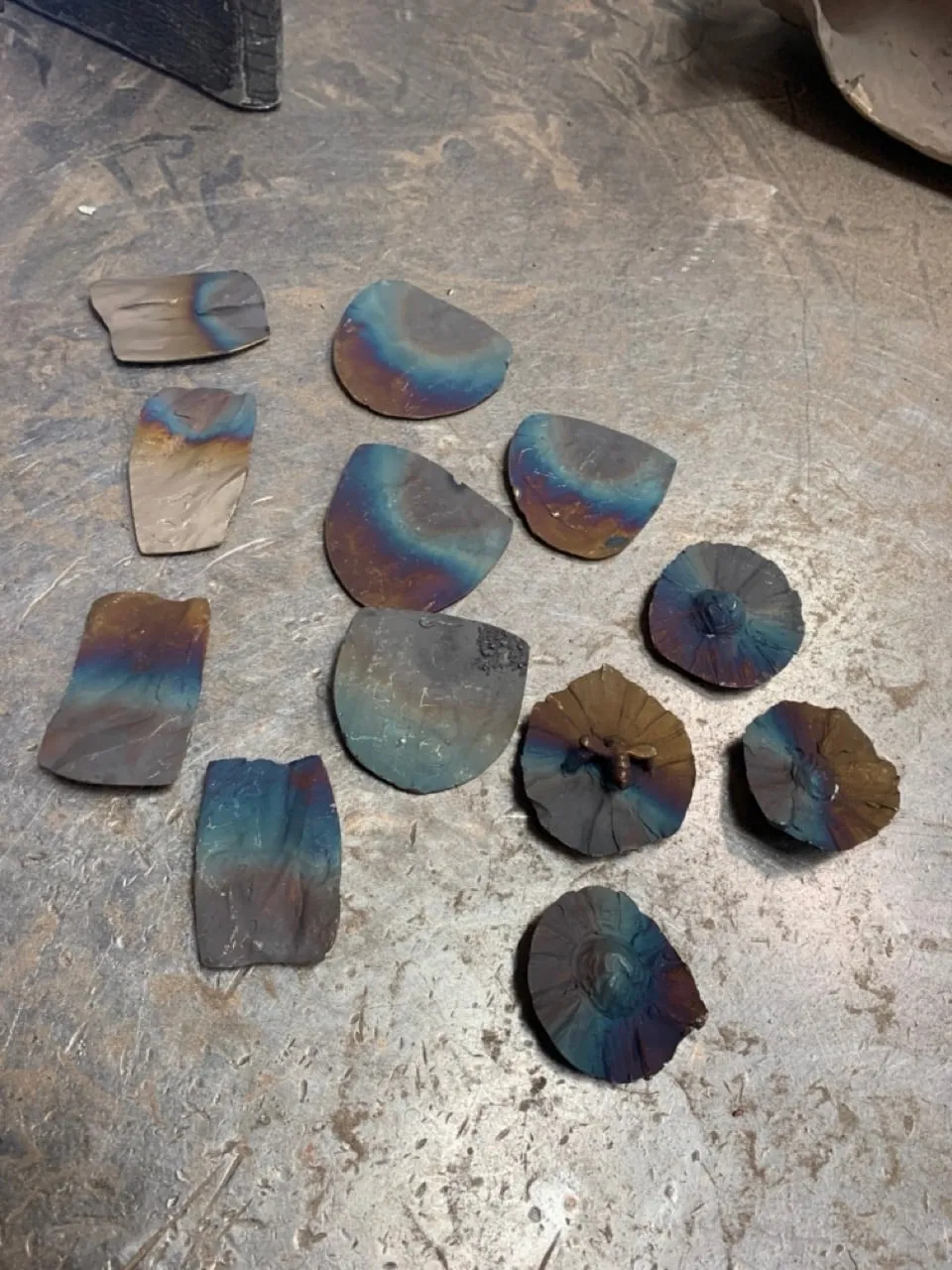 Small bronze test pieces on a steel bench, heat-coloured blue, violet and gold