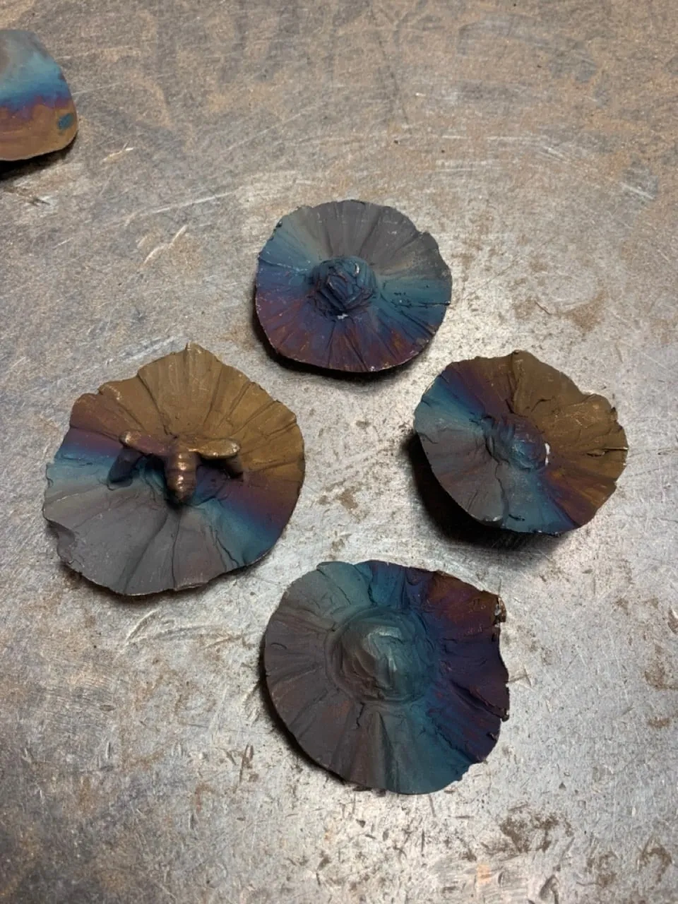Four round bronze test discs with blue and amber heat patina