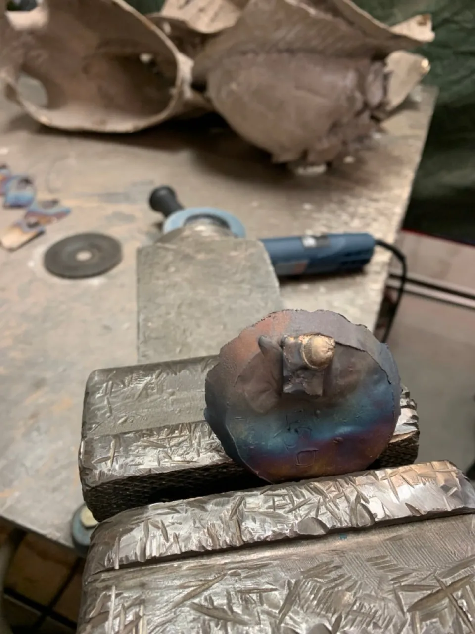 A patinated test disc beside a grinder on the bench