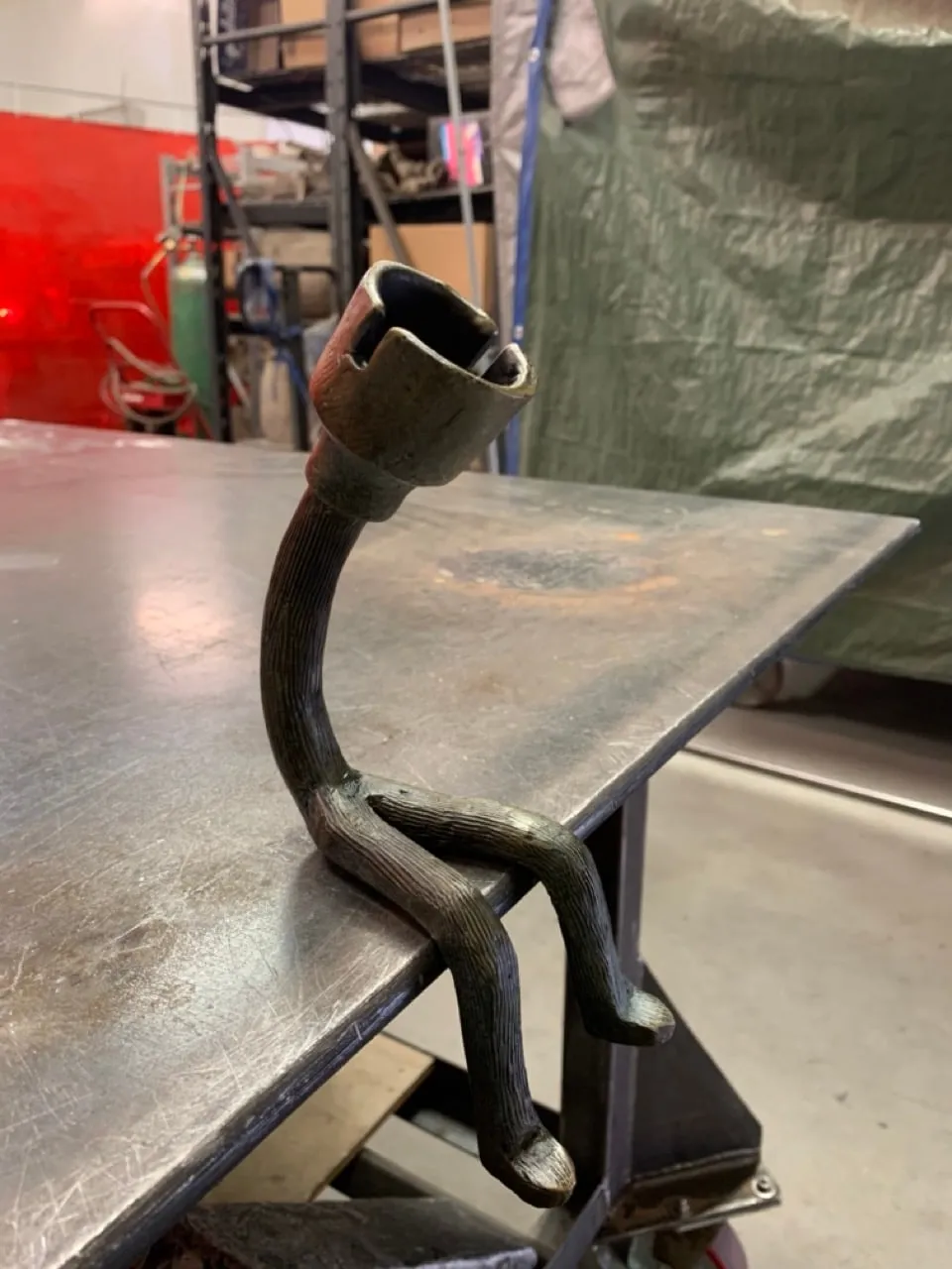 Bronze figure with a lamp-socket head, seated on the edge of a steel workbench