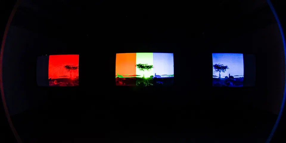 Wide-angle view of the three screens, each showing a lone tree in red, orange-green and blue