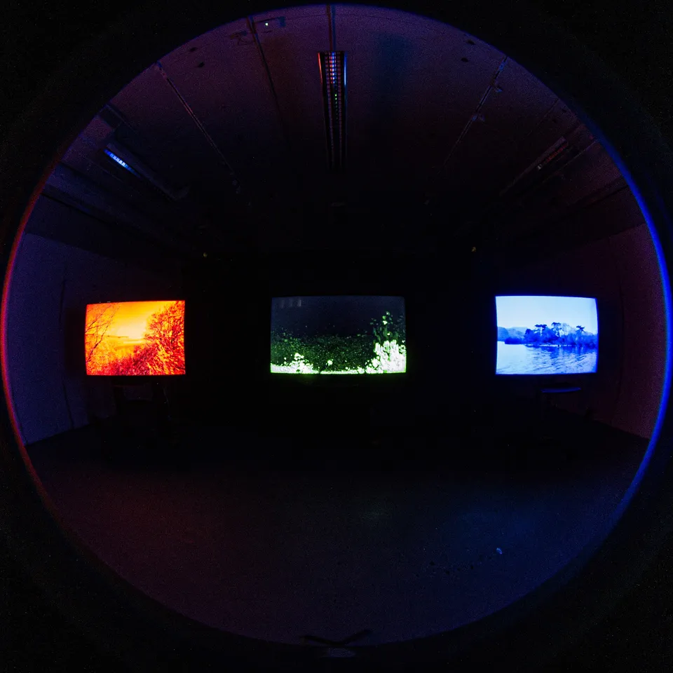 Fisheye view of the darkened room with the three glowing screens on the far wall